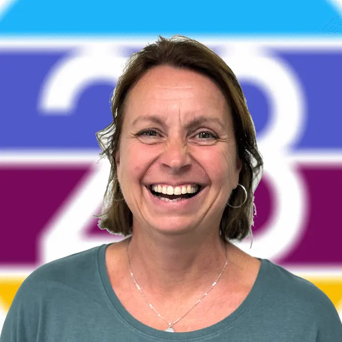 Lächelnde Frau mit kurzen braunen Haaren und einem grünen Oberteil vor einem bunten Hintergrund.